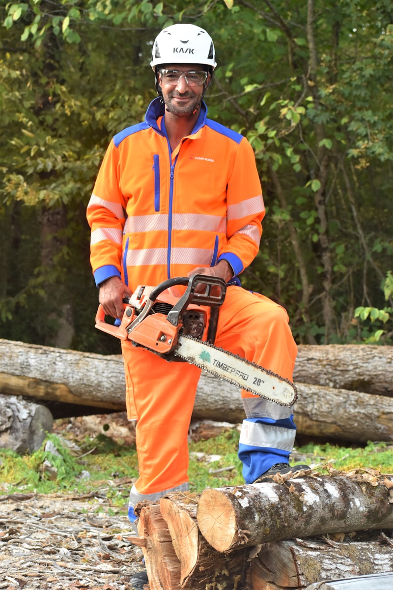 a man in an orange safety suit with contractors insurance holding a chainsaw