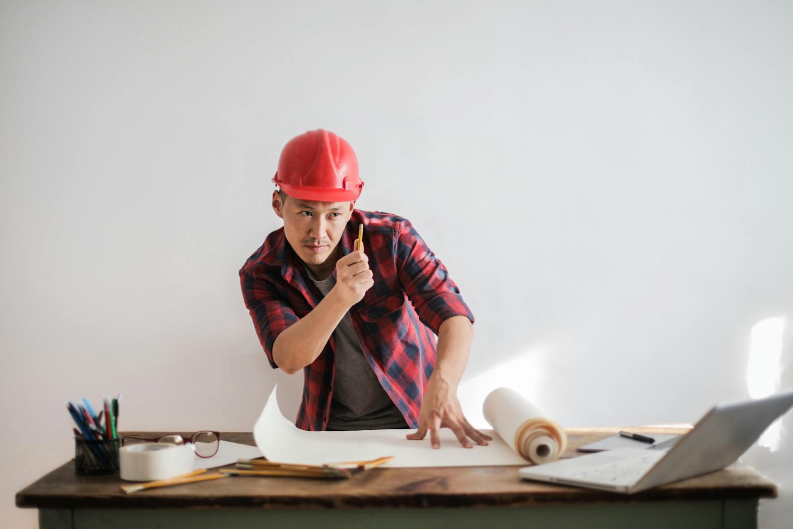 Asian engineer in hard hat reviewing plans with focus and determination in a bright office.